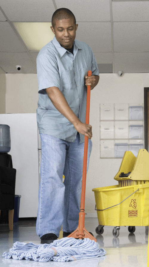 A janitor using a mop and bucket to wash the hallway floor of an office corridor in a Manhattan building.