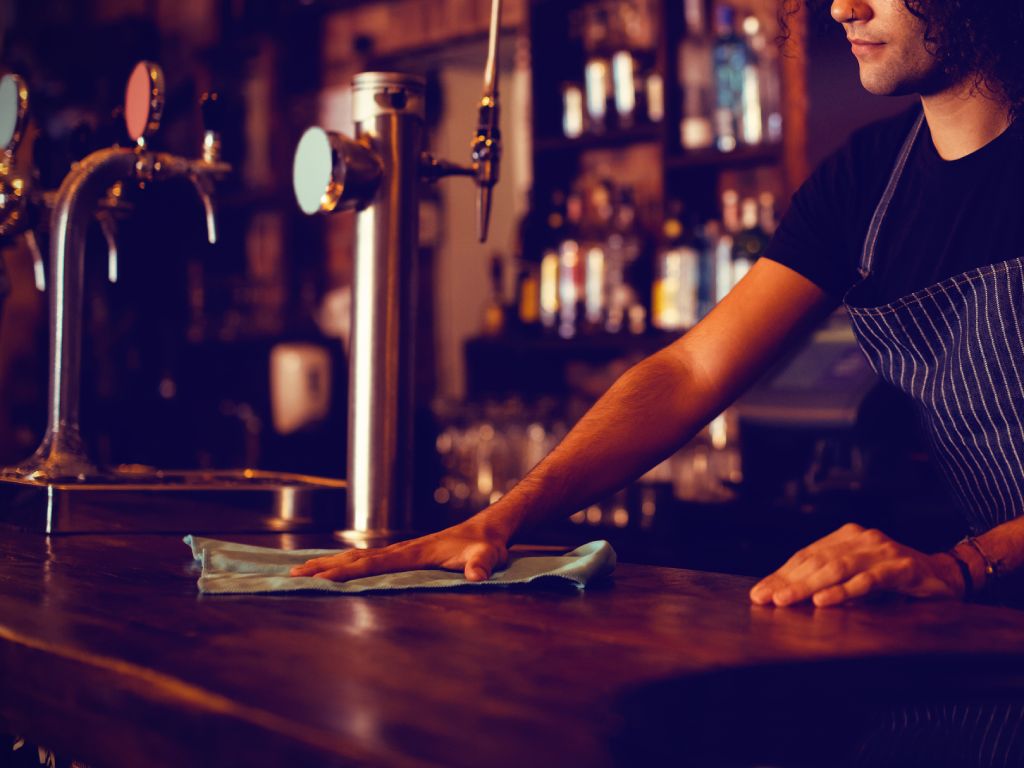 Pub porter cleaning services, NYC. Bar cleaning staff wipes down counters.